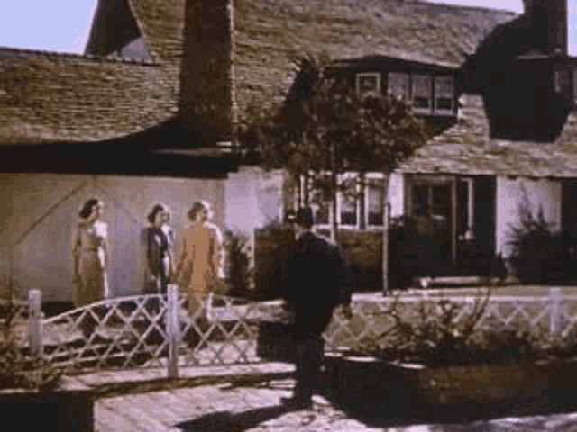 a group of people are walking across a wooden bridge in front of a house .