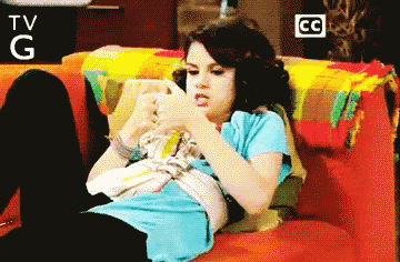 a woman laying on a couch looking at her phone with a tv g and cc logo behind her