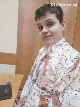 a young man wearing a shirt with cats on it is sitting at a table