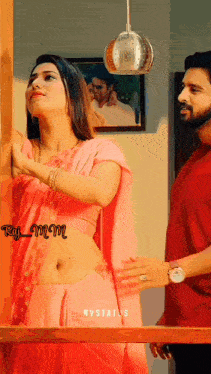 a woman in a pink saree stands next to a man in a red shirt ..