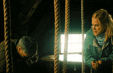 a woman in a green jacket stands next to a man in a green jacket behind ropes