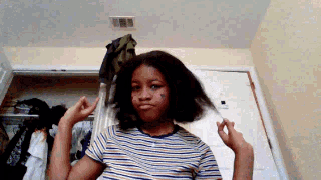 a girl in a striped shirt is holding her hair in front of a closet