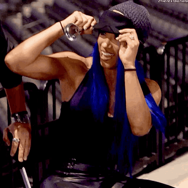 a woman with blue hair is smiling and wearing a hat