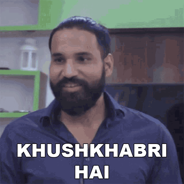 a man with a beard and a blue shirt says " khushkhabri hai "