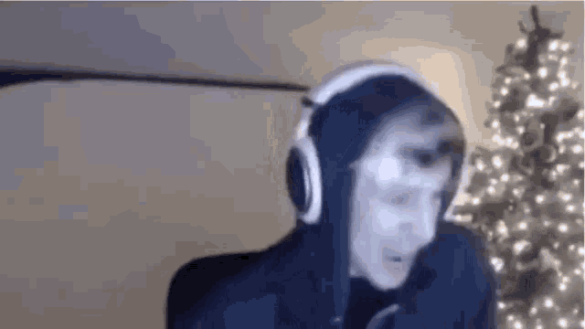 a man wearing headphones and a hoodie is standing in front of a christmas tree .