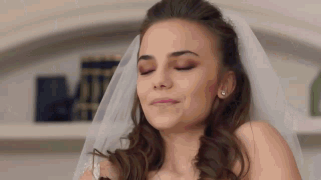 a bride in a wedding dress and veil with her eyes closed is smiling .