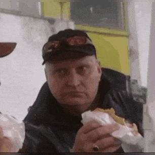 a man wearing sunglasses and a hat is eating a sandwich .