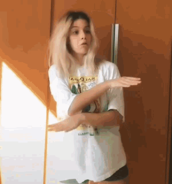 a woman in a white t-shirt and black shorts is dancing in front of a wooden wall .