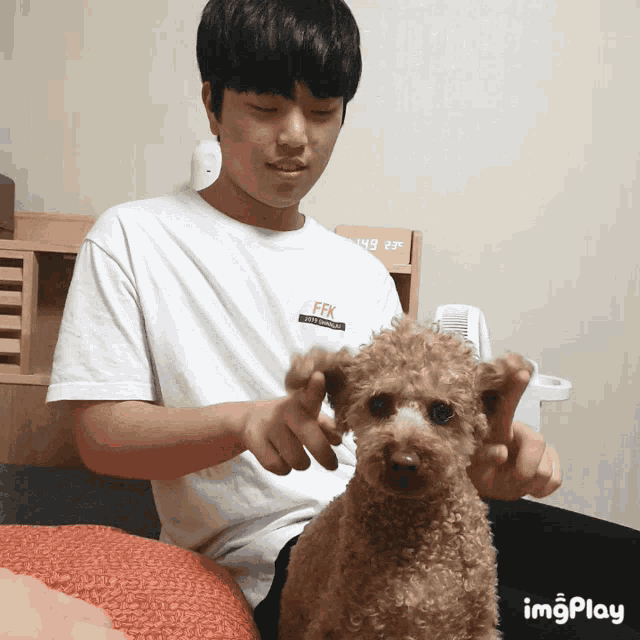 a man with a white shirt that says ffk is playing with a small brown dog
