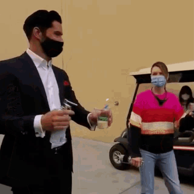 a man wearing a mask is holding a cup of coffee while standing next to a woman wearing a mask .