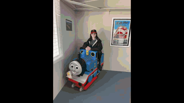 a man is sitting on a thomas train in front of a poster of a train