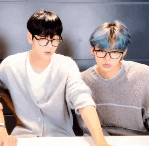 two boys wearing glasses and sweaters are sitting at a table