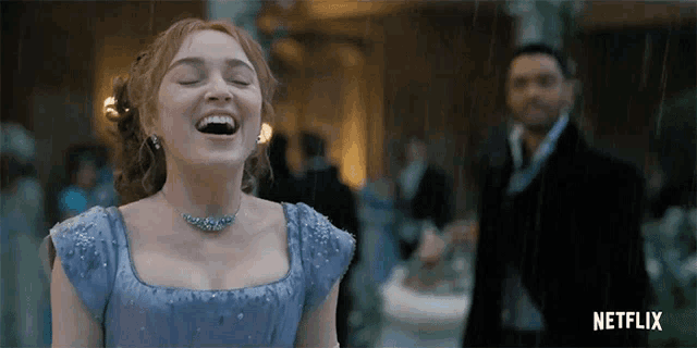 a woman in a blue dress is laughing in the rain while a man in a black suit stands behind her .