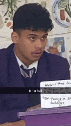 a man in a suit and tie is sitting in front of a purple box that says 8 n a half