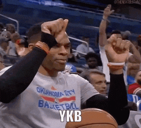 a man in an oklahoma city basketball shirt is sitting in the stands with his hands in the air