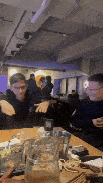 a man wearing glasses sits at a table with a pitcher of water and a card that says balance on it