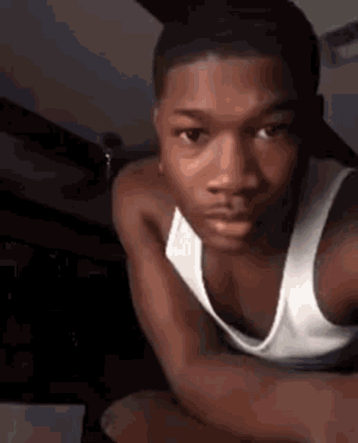 a young man wearing a white tank top is taking a selfie with his phone .