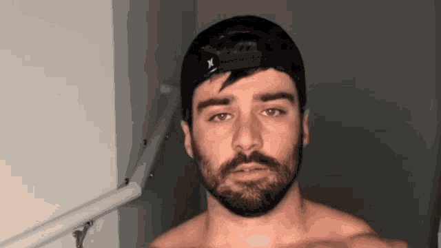 a shirtless man with a beard and a hat is standing in a dark room .