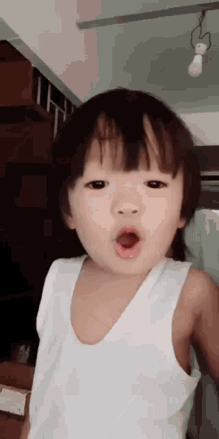a little boy is wearing a white tank top and making a surprised face .