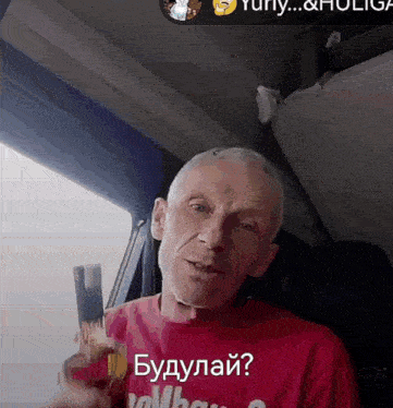 a man wearing a red shirt that says " будулай " holds a bottle