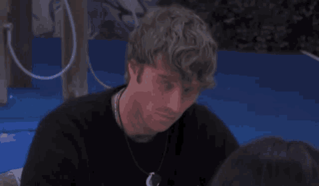 a man with curly hair is sitting next to a woman on a blue surface and making a funny face .