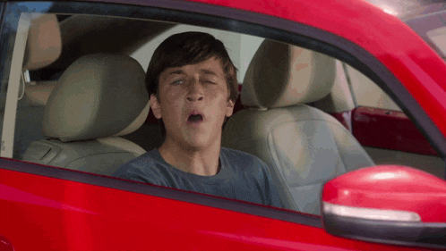 a young man is yawning while sitting in a red car