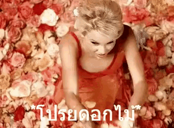a woman in a red dress is laying in a pile of roses petals .