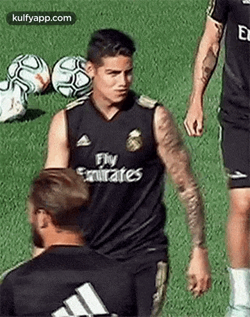a soccer player wearing a fly emirates jersey is standing on a field with soccer balls .