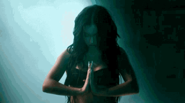 a woman with long black hair is standing in a dark room with her hands folded .
