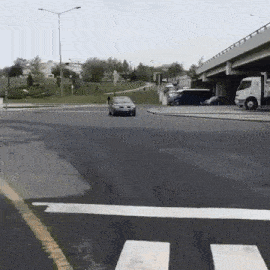 a car is driving down a street next to a truck and a bridge .