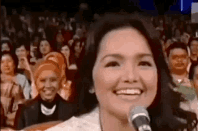 a woman is smiling while singing into a microphone in front of a crowd of people .