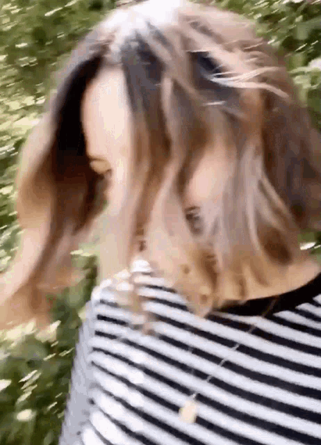 a woman wearing a striped shirt is blowing her hair in the wind .
