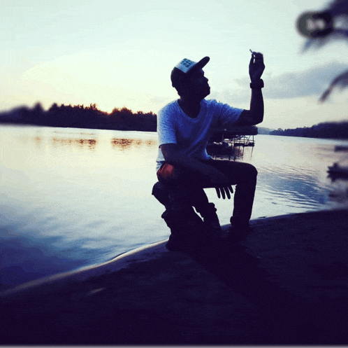 a man taking a picture of a body of water with a hat that says ' columbia ' on it