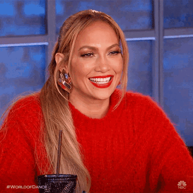 a woman wearing a red sweater is smiling while holding a drink in her hand .