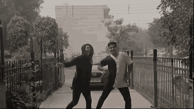 a man and woman are dancing in front of a red nissan