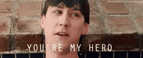 a man is standing in front of a brick wall and says you 're my hero
