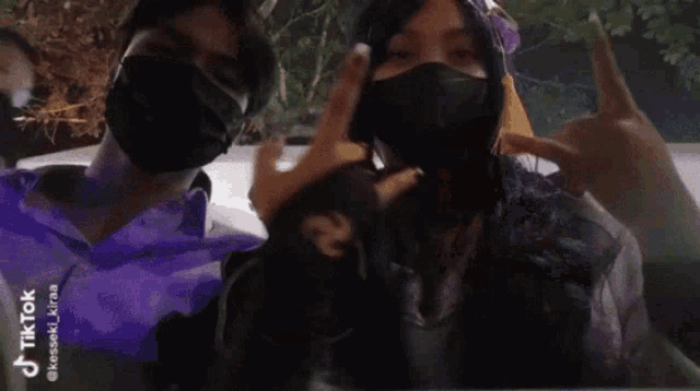 a man and a woman wearing face masks are making a peace sign