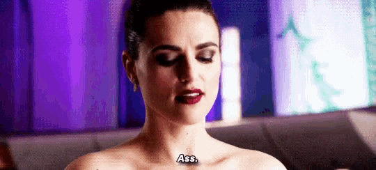 a woman without a shirt is sitting on a couch with a tattoo on her chest that says `` ass '' .