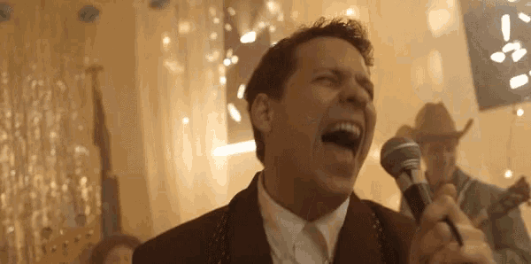 a man is singing into a microphone with a cowboy in the background