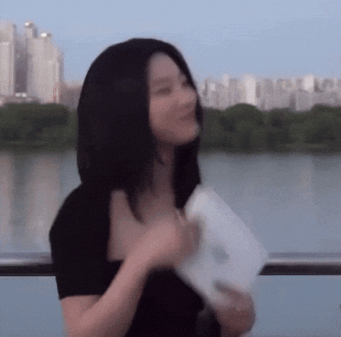 a woman is holding a piece of paper in front of a lake .