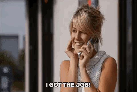 a woman is smiling while talking on a cell phone and says i got the job .