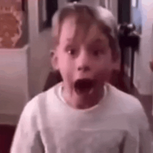 a young boy is making a surprised face while wearing a hat and a white shirt .