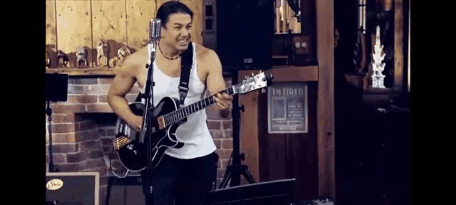 a man without a shirt is playing a guitar in front of a microphone in a room .