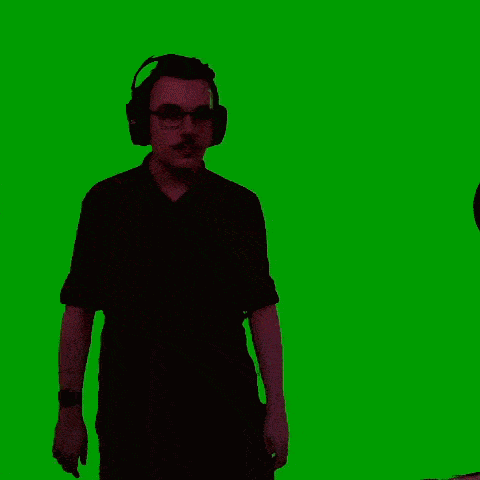a man wearing headphones and a mustache is standing in front of a green screen .