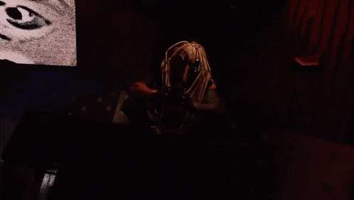a man with dreadlocks sits in a dark room with blue lights