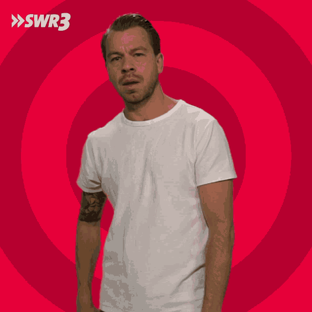 a man in a white t-shirt is standing in front of a red circle with the letters swr3 on it