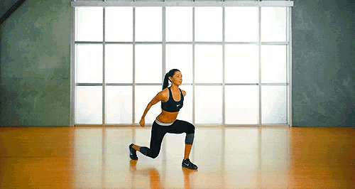 a woman is doing lunges in a gym with a lot of windows .