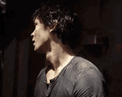 a man with curly hair is standing in a dark room looking up .
