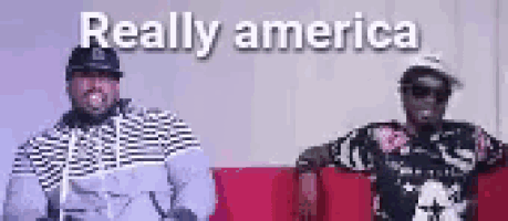 two men are standing next to each other on a red couch with the words really america written on the bottom .