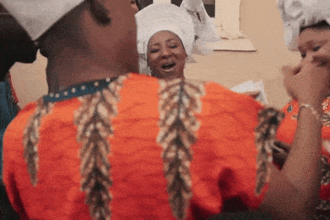 a man in an orange shirt with feathers on the sleeves is standing next to a woman in a white turban